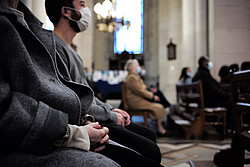 Gottesdienstbesucher sitzen in der Kirchenbank, tragen eine Mund-Nase-Bedeckung und falten die Hände. 