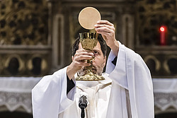 Priester hält Hostie und Kelch hoch