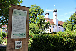 Stele mit Infos zum Heiligen Benedikt,im Hintergund das Kloster Benediktbeuern