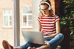 Junge Frau mit Kopfhörern arbeitet zuhause am Laptop