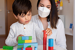 Frau mit Maske spielt mit Kind