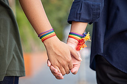 Zwei Männer halten Händchen, beide tragen ein Armband mit Regenbogenfarben.