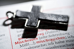 Kreuz liegt auf Wörterbuch, mit aufgeschlagener Seite zum Eintrag "Missbrauch"