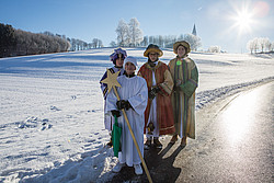 Vier Stermsinger im Schnee, im Hintergrund eine Kirche