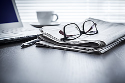 Brille liegt auf Zeitung, Laptop und Kaffetasse im Hintergrund