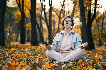 Frau meditiert im Wald mit Kopfhörer und Handy