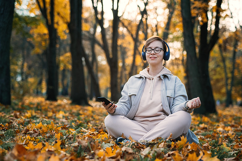 Frau meditiert im Wald mit Kopfhörer und Handy