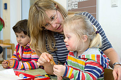 Eine Erzieherin bastelt mit einem Mädchen mit Down-Syndrom in einer integrativen Gruppe in einem Kindergarten.